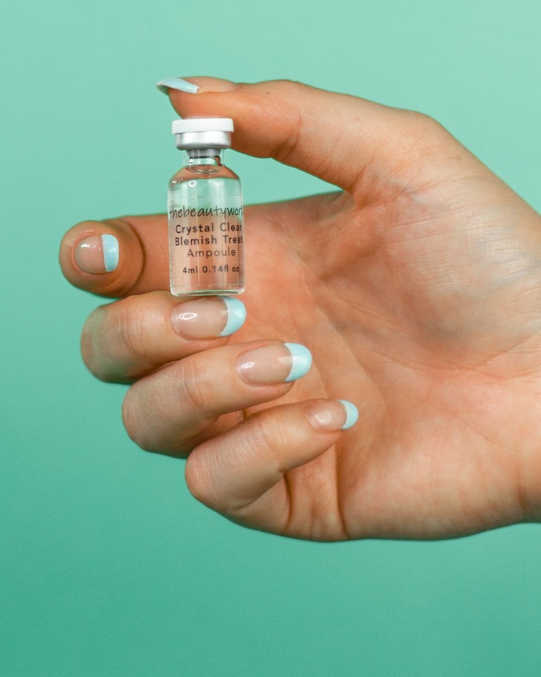A hand holding a thebeautyworX blemish treatment ampoule against teal