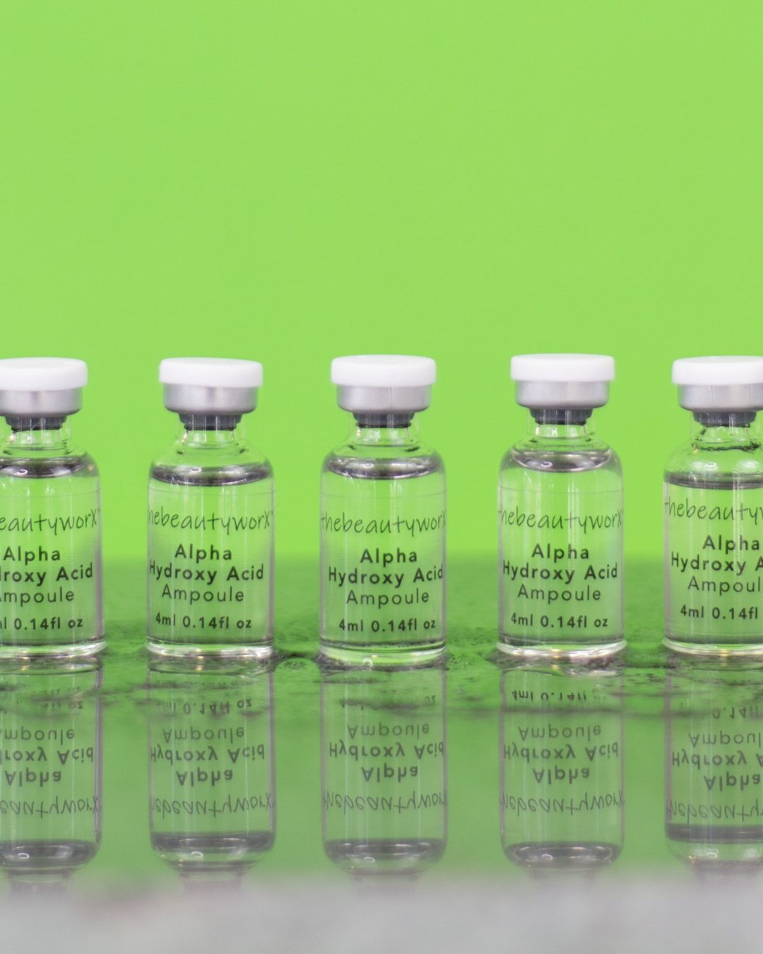 A row of thebeautyworX Alpha Hydroxy Acid ampoules on bright green, reflected in water