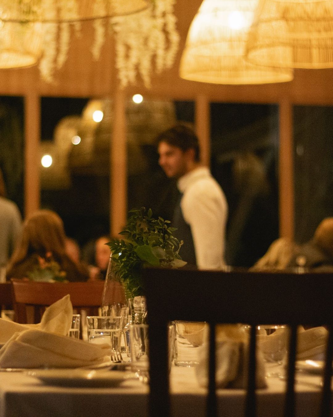 Val De Vine: the dining room at night under woven pendant lights, a waiter between the tables